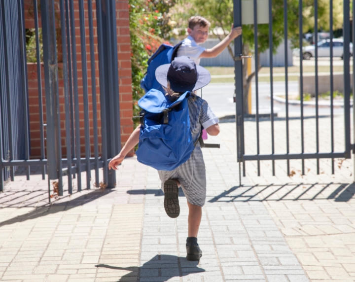 Enfant courant vers un portail, vu de dos, avec son sac à dos