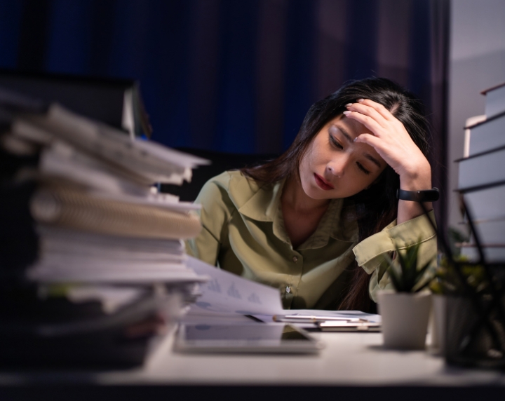 Salariée à son bureau, la main sur le front, entourée de dossiers